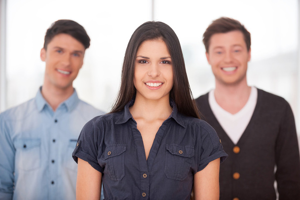 Attractive young woman smiling while two men standing behind her - Foto, imagen