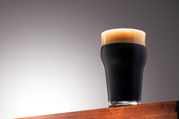 Feche a foto de um copo de cerveja escura em uma superfície de madeira e fundo de gradiente com Clipping Path - Foto, Imagem