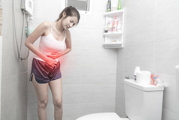 Young woman suffering from strong abdominal pain while standing in restroom. - Photo, Image