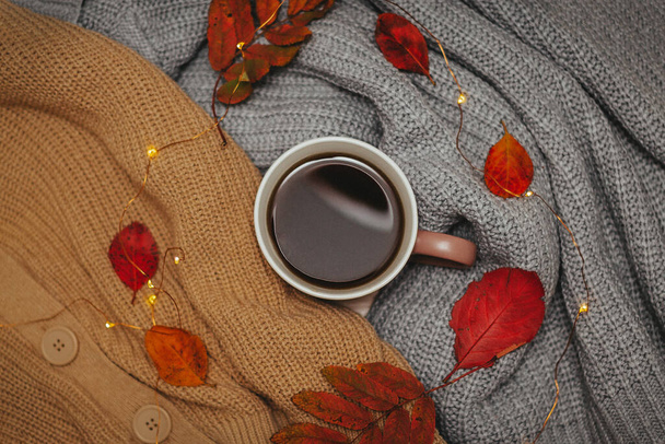 autumn, dry red autumn leaves lie on sweaters that are stacked around a hot espresso mug, around lies a led garland, Flatley - Φωτογραφία, εικόνα