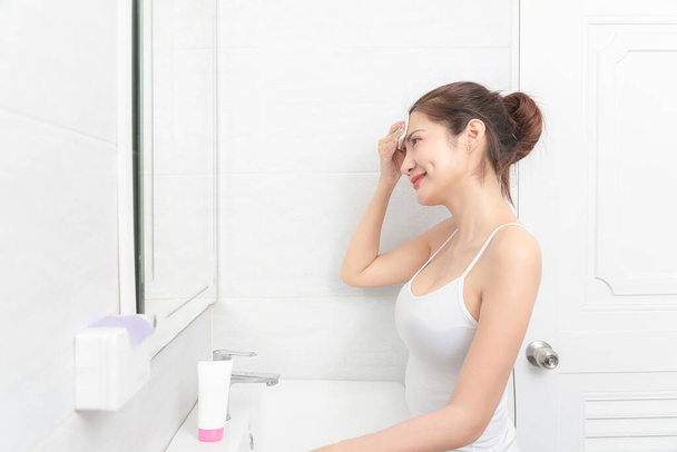 鏡の中に化粧品クリームの反射を適用する美しいアジアの女性. - 写真・画像