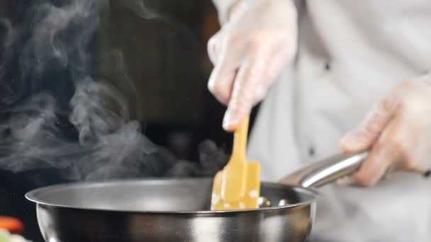 Eten koken in restaurant. Een slow motion video. Vrouwelijke chef-kok in handschoenen en wit uniform roeren voedsel met peddel in koekenpan. Traditionele mediterrane keuken. Vol hd - Video