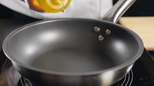 Warme koekenpan op het fornuis. Olie gieten in slow motion. Koken. Chef giet zonnebloemolie in koekenpan, macro shot. Olijfolie wordt gegoten. Vol hd - Video
