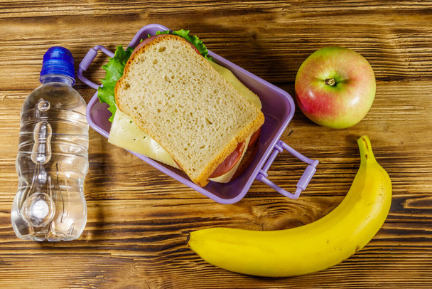 Lunchbox mit Sandwiches, Flasche Wasser, Banane und Apfel auf einem Holztisch. Ansicht von oben - Foto, Bild