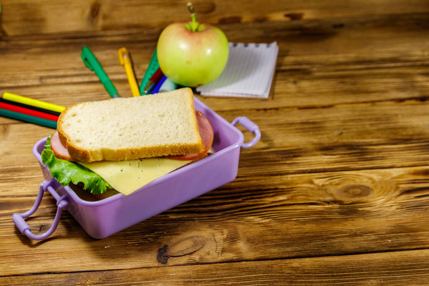 Back to school concept. School supplies, apple and lunch box with sandwiches on a wooden desk - Photo, Image