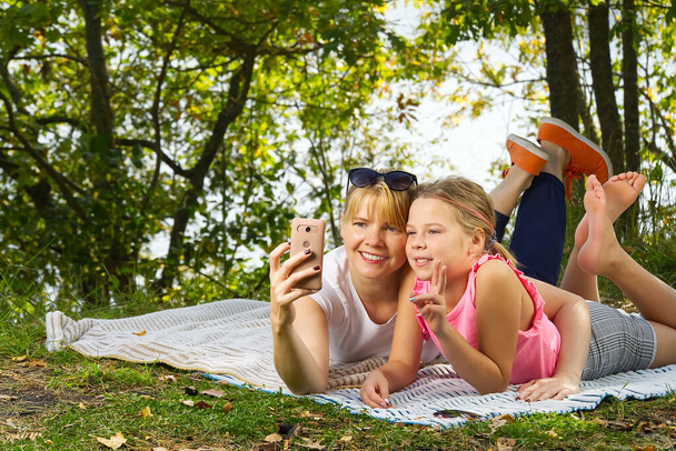 Mère et fille jouent sur une couverture dans la forêt d'automne près de la rivière ou du lac. Jeune mère jouant avec sa fille dans le parc d'automne par une journée ensoleillée. Le concept des relations familiales et des enfants - Photo, image