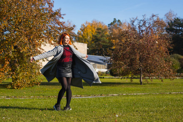 Mladá žena v teplém podzimním oblečení se těší teplému slunci a víří v městském parku za teplého podzimního dne - Fotografie, Obrázek