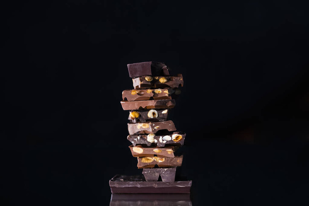Gros plan d'une tour faite de morceaux de chocolat assortis avec des amandes et des noisettes sur un fond sombre flou. Concept de dessert. - Photo, image