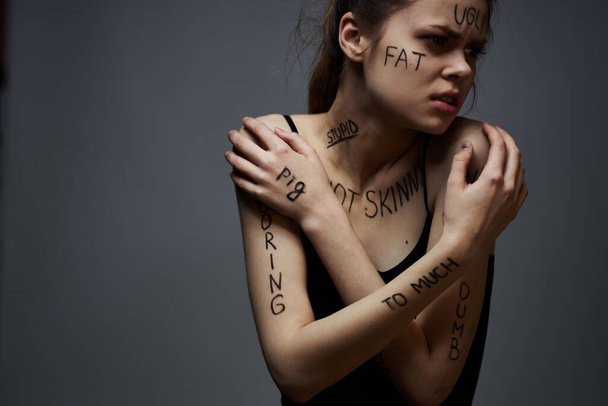 Emotionale Frau mit Inschriften auf ihrem Körper Gesten mit Händen Lebensstil Frustration Stress grauer Hintergrund - Foto, Bild