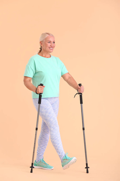 Mature woman with walking poles on color background - Fotografie, Obrázek