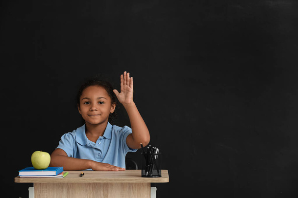 暗い背景を背景に学校の机に座っている小さなアフリカ系アメリカ人の生徒 - 写真・画像