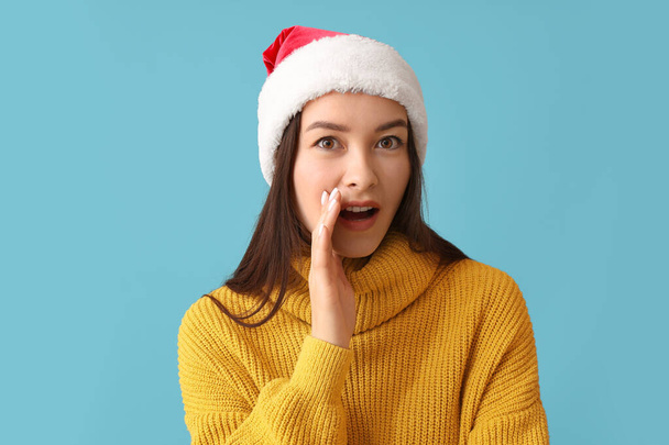 Klatschende junge Frau mit Weihnachtsmütze auf farbigem Hintergrund - Foto, Bild