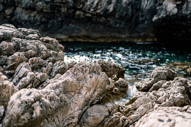 Rocallosas rocas masivas cerca de agua de mar azul y montañas. - Foto, imagen