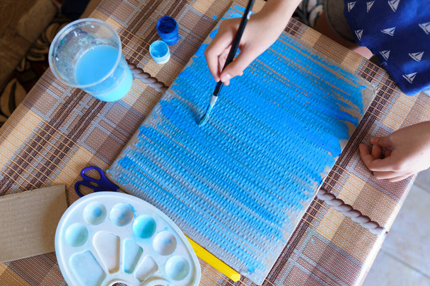 het meisje tekent blauw gouache karton, maakt een achtergrond, zit in de huiskeuken - Foto, afbeelding