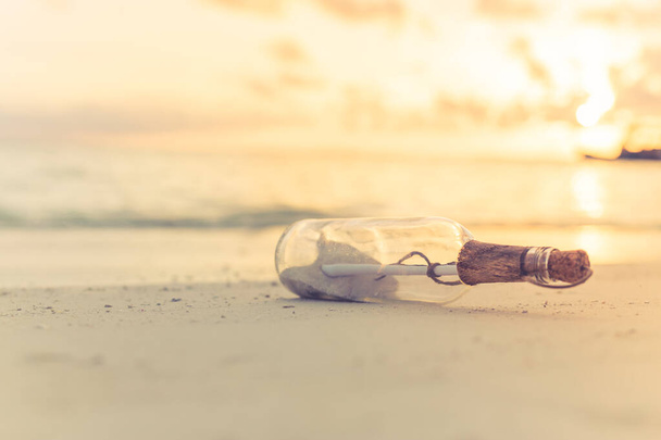 Message in the bottle washed ashore against the sun setting down. Tropical beach design background, message in a bottle on a sea shore - Photo, Image