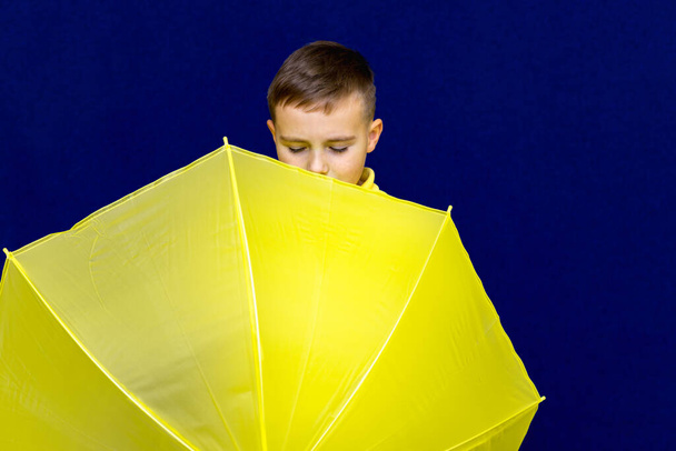 Attractive surprised caucasian blond schoolboy scatter umbrellas hiding on him.Boy shows all kinds of grimaces. - Foto, Imagem