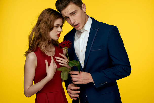 Un homme romantique étreint une femme dans une robe rouge avec une rose à la main sur un fond jaune - Photo, image