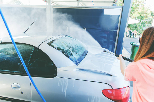 Mooie vrouw wassen haar auto met hoge druk Wasmachine bij Self-Serve Car Wash  - Foto, afbeelding