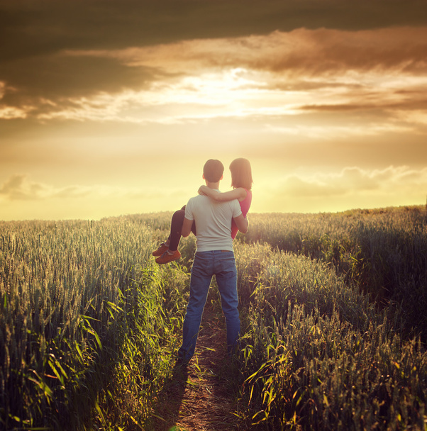 Hombre lleva a la mujer en el campo de verano en la puesta del sol
 - Foto, Imagen