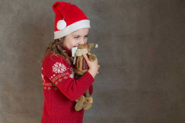 Malá šťastná dívka v vánoční bundě a Santa klobouk se Santa Claus hračka - Fotografie, Obrázek