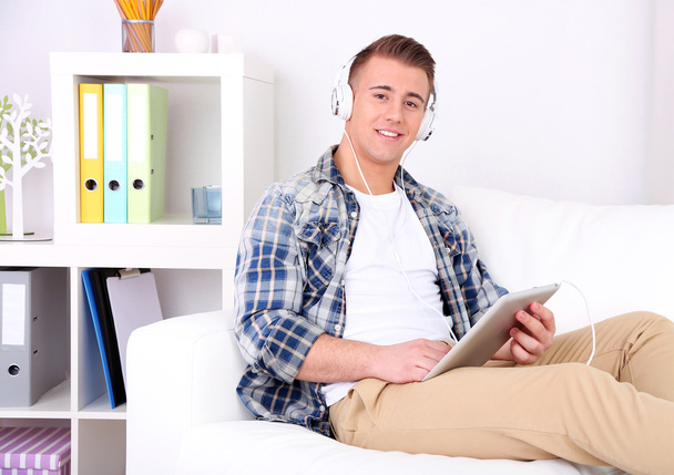 przystojny młody mężczyzna siedzi na kanapie i słuchanie muzyki w pokoju - Zdjęcie, obraz