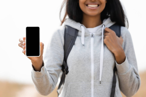 Smartphone with blank screen in hand of african american woman with backpack on blurred background outdoors  - Foto, Bild