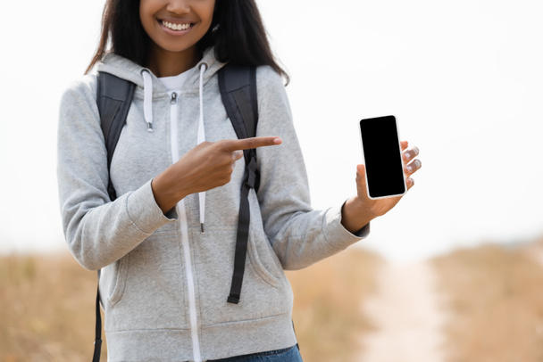 Cropped view of smiling african american tourist pointing with finger at smartphone with blank screen outdoors  - Zdjęcie, obraz