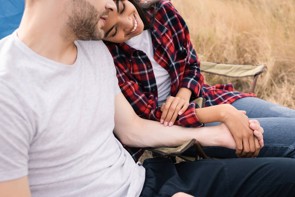 Smiling african american woman holding hand of boyfriend during camping on lawn  - Photo, Image