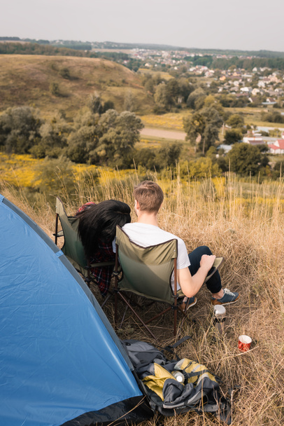 バックパックやテントの近くに芝生の上に座って観光客のバックパックビュー  - 写真・画像