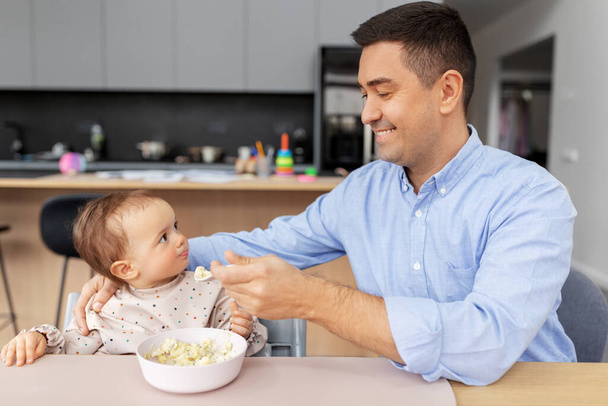 happy father feeding baby in highchair at home - Photo, Image