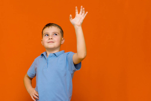 Portarait of caucasian happy smiling little boy with raised hand on orange studio wall - Foto, afbeelding