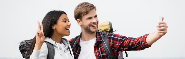 Smiling multiethnic travelers talking selfie with smartphone on grey background, banner  - Foto, imagen