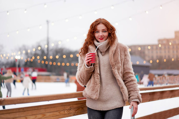 Young beautiful redhead girl freckles ice rink background Pretty woman curly hair portrait walking new year fair Modern cute female skate ice rink  chrismas holiday decorated street.  - Fotó, kép
