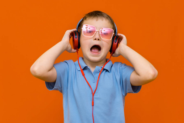 atraktivní mladý kluk nosí červené brýle je poslech hudby s červenými sluchátky na oranžovém pozadí studia - Fotografie, Obrázek