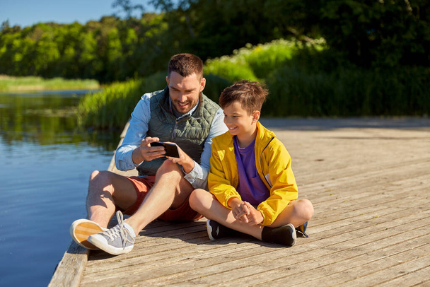father and son with smartphone on river berth - Foto, imagen