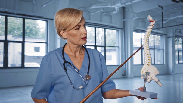 μεσήλικας γιατρός μιλάει και κρατώντας το ραβδί κατάδειξης κοντά στο σκελετό  - Πλάνα, βίντεο
