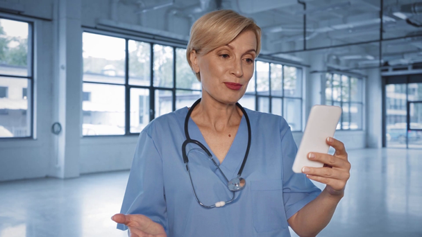 ευτυχής μεσήλικας γιατρός κρατώντας smartphone, ενώ έχοντας βιντεοκλήση - Πλάνα, βίντεο