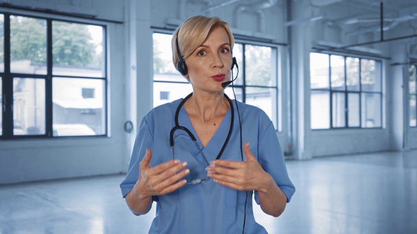 médico de meia idade falando em fone de ouvido no centro médico  - Filmagem, Vídeo