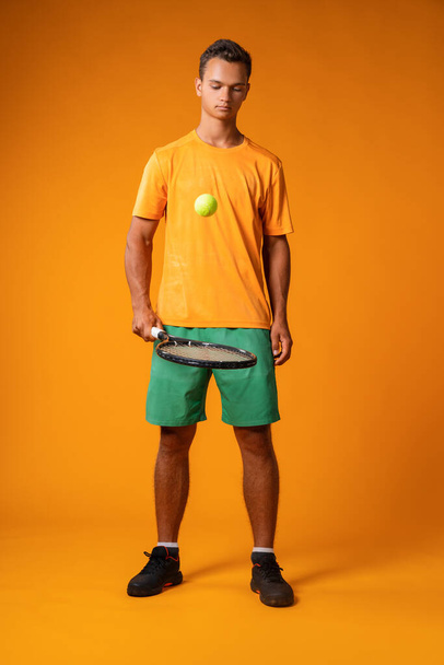 Full-length portrait of a tennis player man in action against orange background - Foto, afbeelding