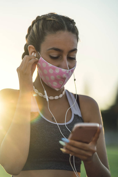A vertical shot of a woman listening to music on her phone while wearing a facemask - Fotoğraf, Görsel