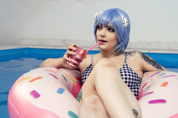 A European female with blue hair drinking a cocktail on an inflatable in a pool - Foto, immagini