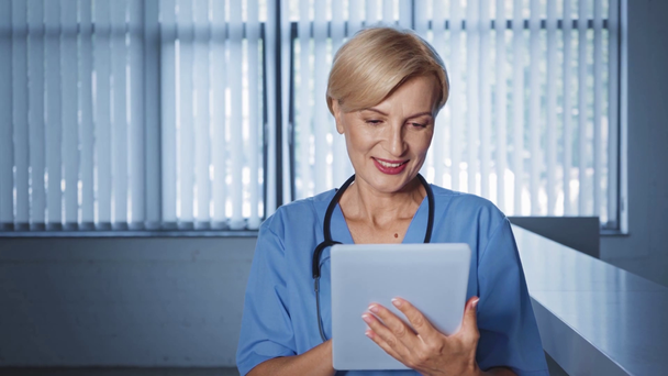 középkorú orvos segítségével digitális tabletta és mosolygós, miközben félrenéz - Felvétel, videó