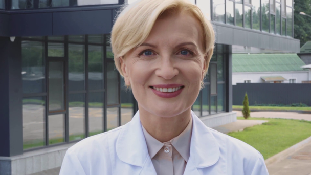 ευχαριστημένος μεσήλικας γιατρός σε λευκό παλτό στέκεται έξω - Πλάνα, βίντεο