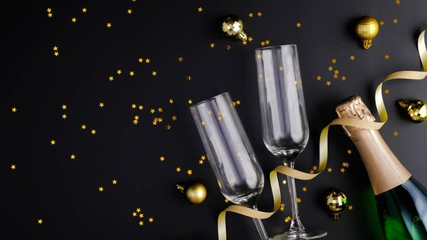 Christmas holiday composition. Christmas champagne, glasses, golden decorations and confetti on black background with copy space. Banner mockup, greeting card. Flat lay, top view, overhead - Foto, Bild