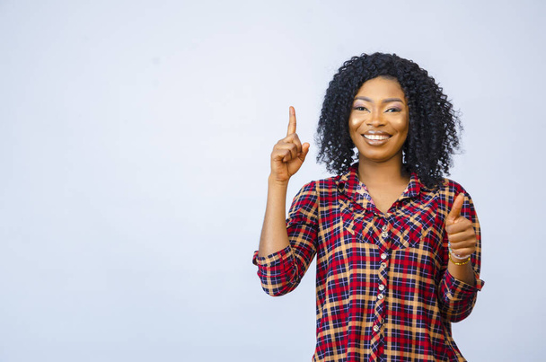 A cheerful African female pointing upward with her thumbs up - Фото, зображення