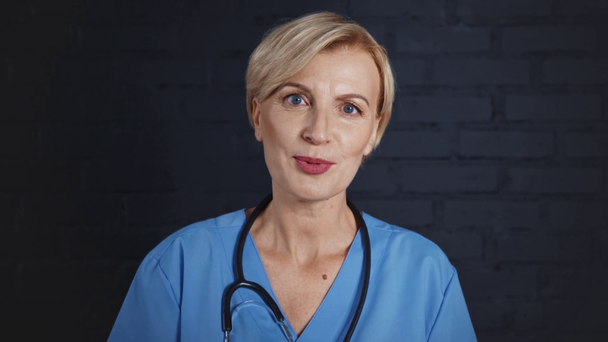 glücklicher und reifer Arzt mit Stethoskop vor Kamera im Krankenhaus  - Filmmaterial, Video