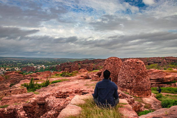 homem meditando no topo da montanha com ruínas do forte histórico no fundo na imagem da manhã é tirada no badami karnataka índia. - Foto, Imagem