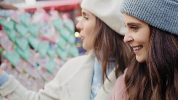 Video kahdesta naisesta kävelemässä ja katselemassa joulumarkkinoiden kojuja. Laukaus punaisella heliumkameralla 8K.   - Materiaali, video