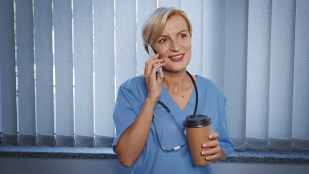 médico maduro feliz segurando copo de papel com café e falando no smartphone - Filmagem, Vídeo