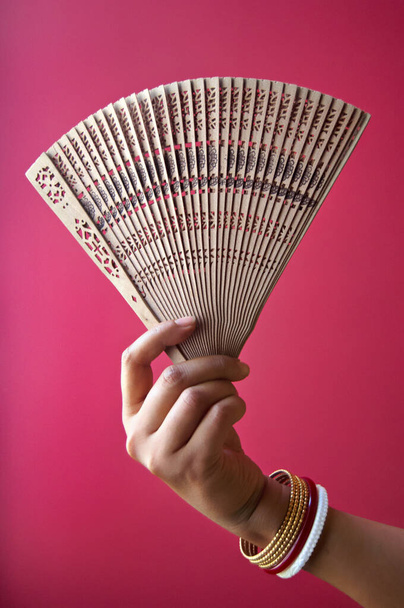 A vertical shot of a woman holding a wooden fan on a pink background - Φωτογραφία, εικόνα
